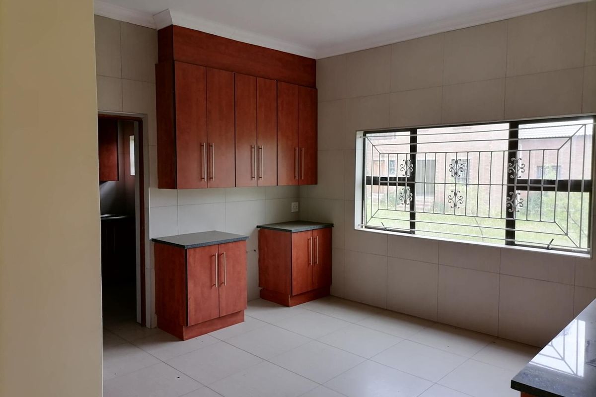 A functional kitchen space featuring wooden cabinetry, tiled walls and flooring, and a large window with security bars.