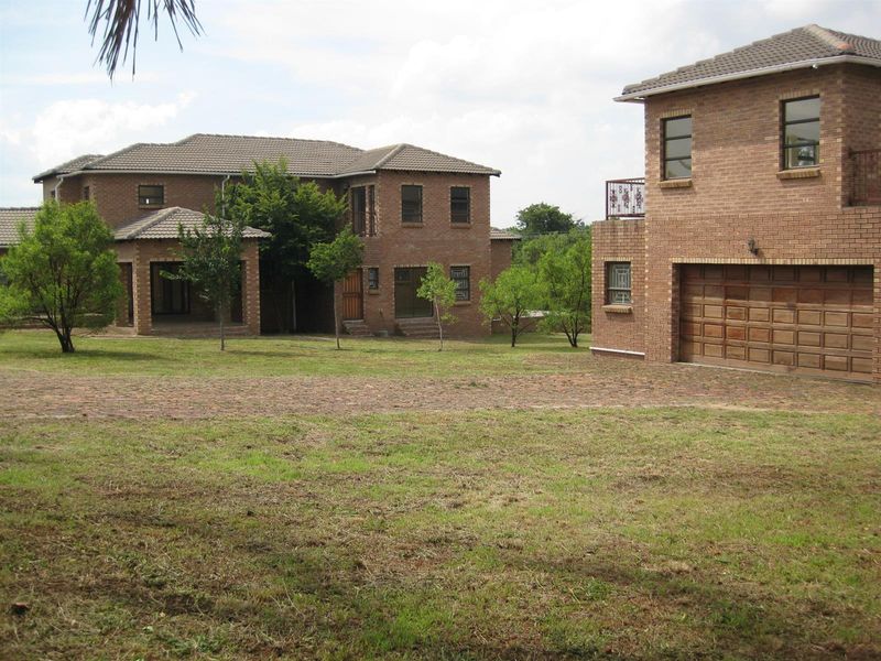 A view of the property exterior featuring multiple brick structures, a paved driveway, and a spacious garden area.