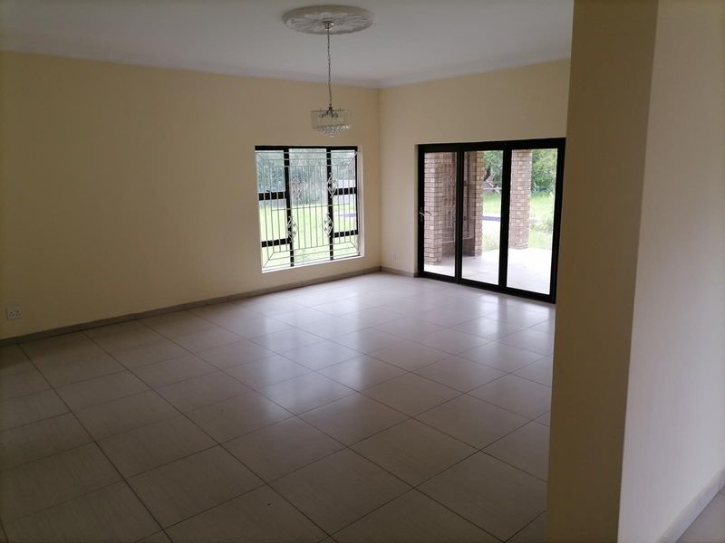 A spacious, empty living area featuring neutral floor tiles, a decorative ceiling rose with a chandelier, and sliding glass doors leading to the patio.