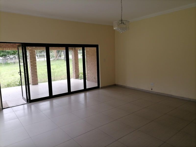 Spacious, light-filled living area featuring large black-framed folding glass doors that open onto a covered brick patio.