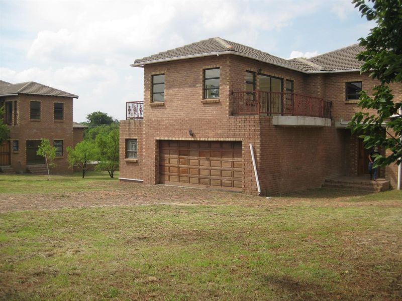 Exterior view of a double-story face-brick house featuring a double garage, upper-level balcony with decorative railing, and tiled roof.