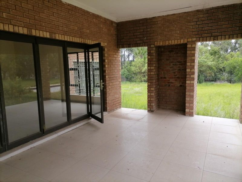 A covered patio area featuring exposed brick walls, tiled flooring, and large glass sliding doors leading to the garden.