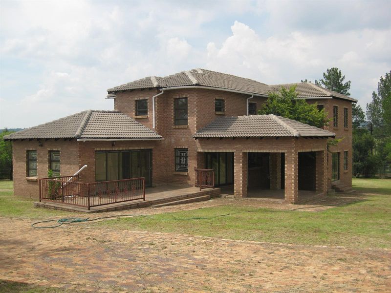 A two-story face-brick house featuring a covered patio, an open deck area with metal railings, and a tiled roof, set within a spacious garden.