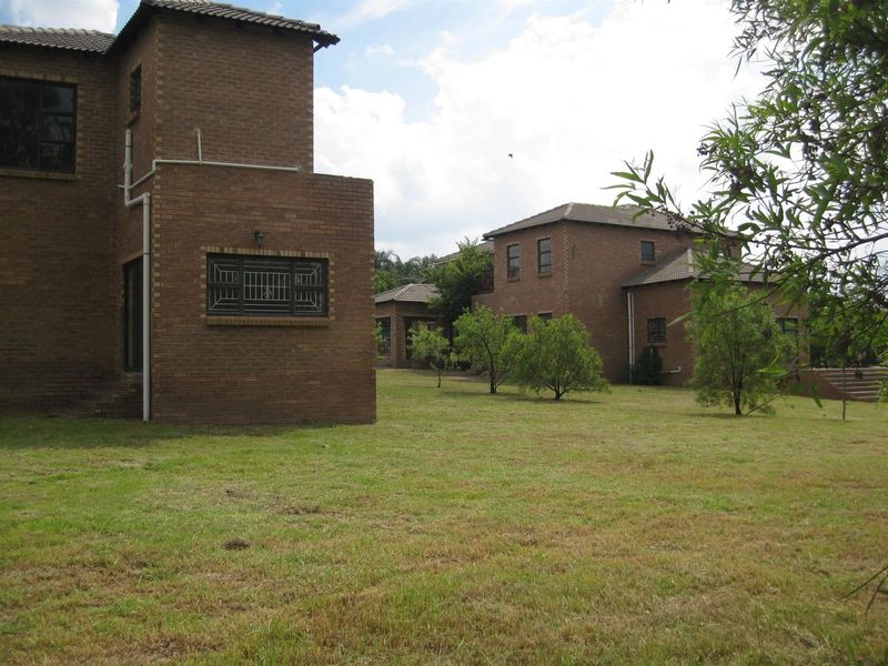 A view of the rear exterior of a multi-story brick house featuring a large garden area and established trees.