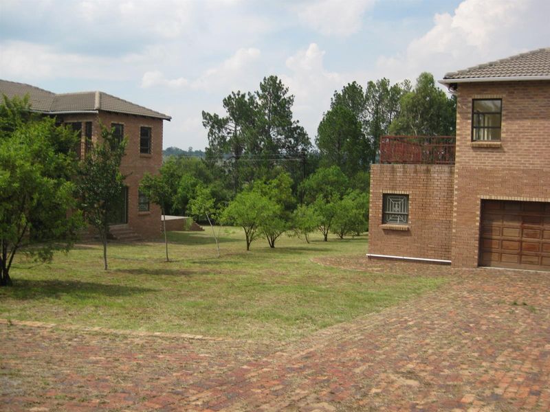 A view of the rear garden area featuring face-brick exterior walls, a paved driveway, and a balcony overlooking the landscaped grounds.