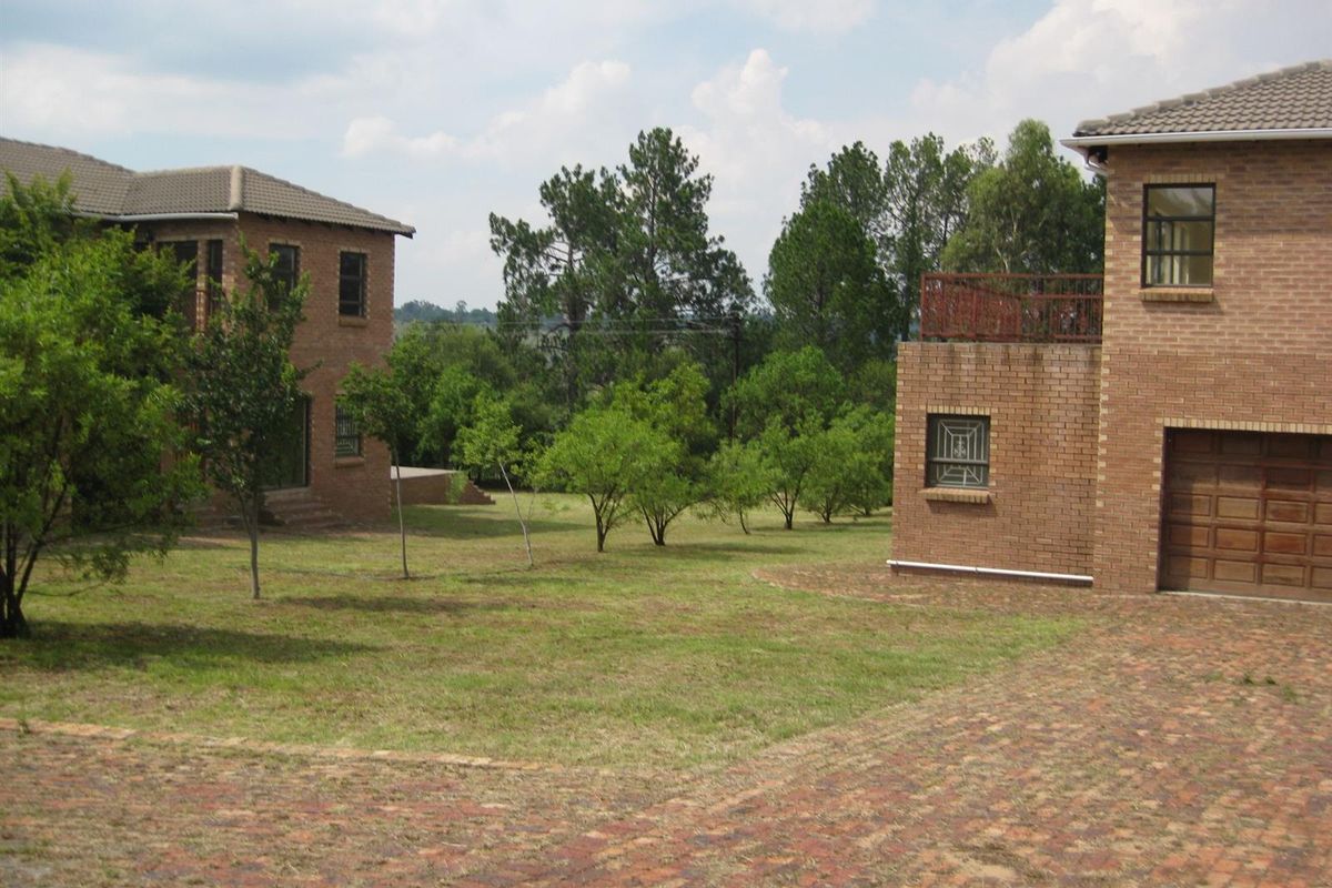 A view of the rear garden area featuring face-brick exterior walls, a paved driveway, and a balcony overlooking the landscaped grounds.