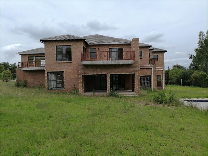 Rear view of a large double-story face-brick house featuring multiple balconies, a covered patio, and an expansive garden area with a pool.