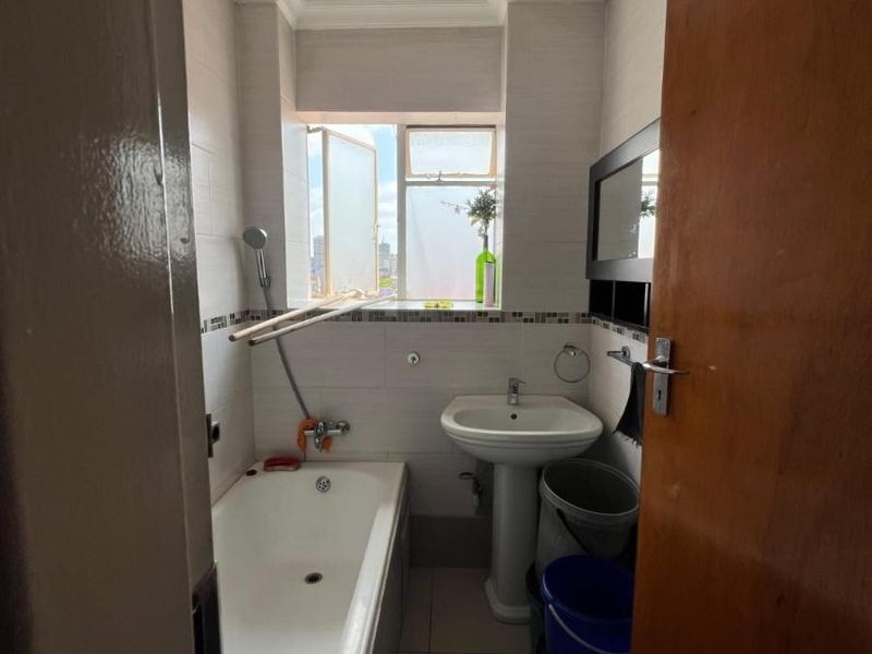 A compact bathroom featuring a pedestal basin, bathtub with shower mixer, and tiled finishes, offering a functional layout with natural light.