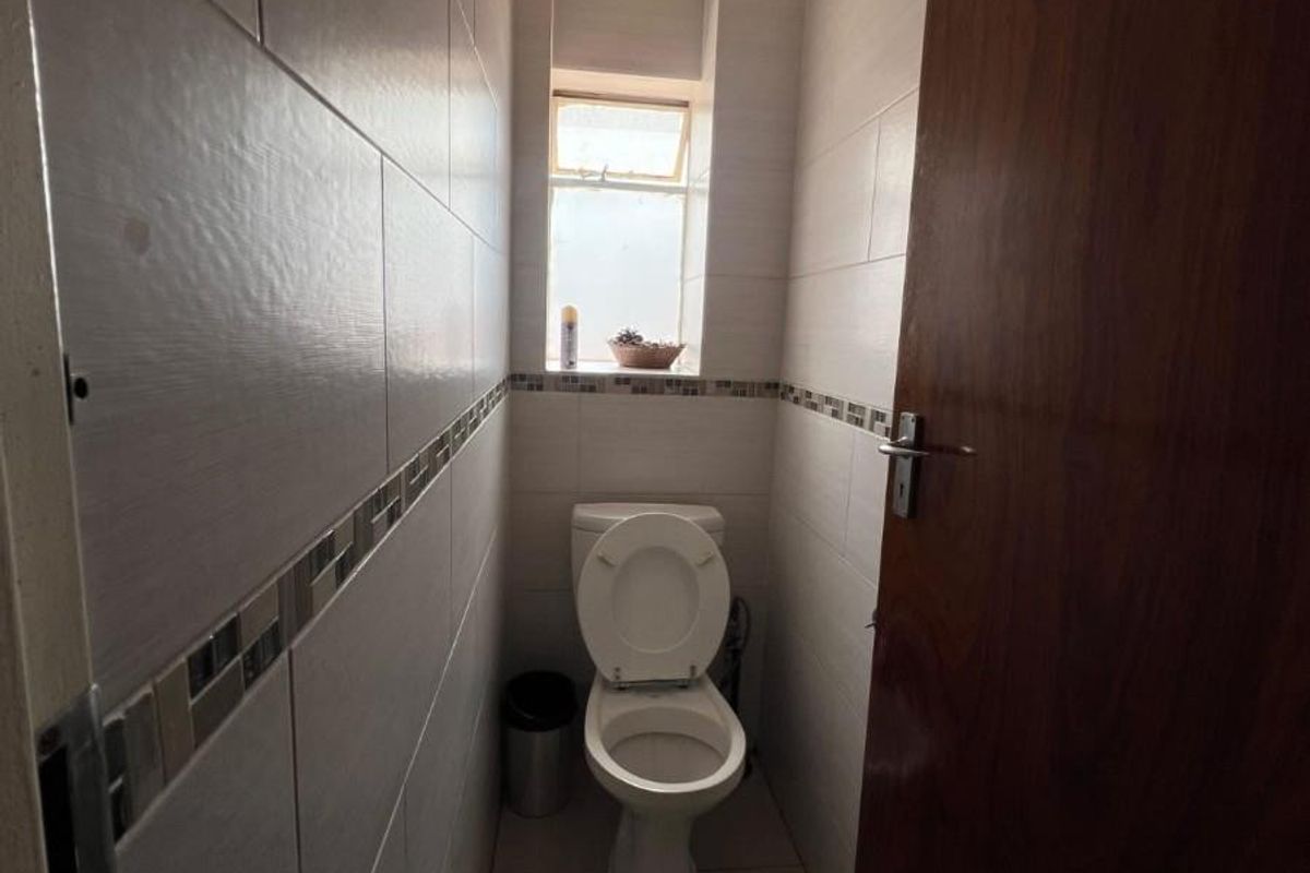A compact guest bathroom featuring neutral wall and floor tiles, a standard toilet, and a window for natural light.