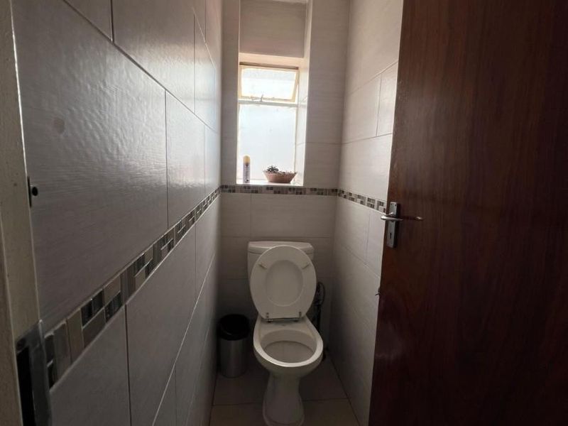 A compact guest bathroom featuring neutral wall and floor tiles, a standard toilet, and a window for natural light.
