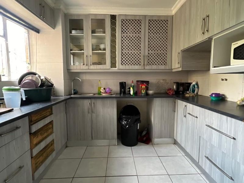A functional kitchen featuring light wood-grain laminate cabinetry, dark countertops, tiled flooring, and ample storage space with a mix of solid and glass-fronted cabinets.