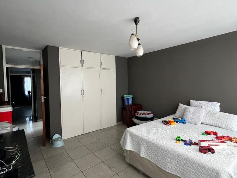 A bedroom featuring tiled flooring, built-in cupboards, and a dark accent wall, providing a functional space with potential for modern updates.