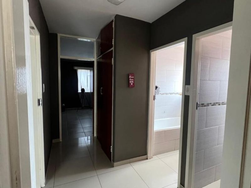 A functional hallway featuring tiled flooring, built-in storage cabinetry, and access to adjacent rooms including a bathroom.
