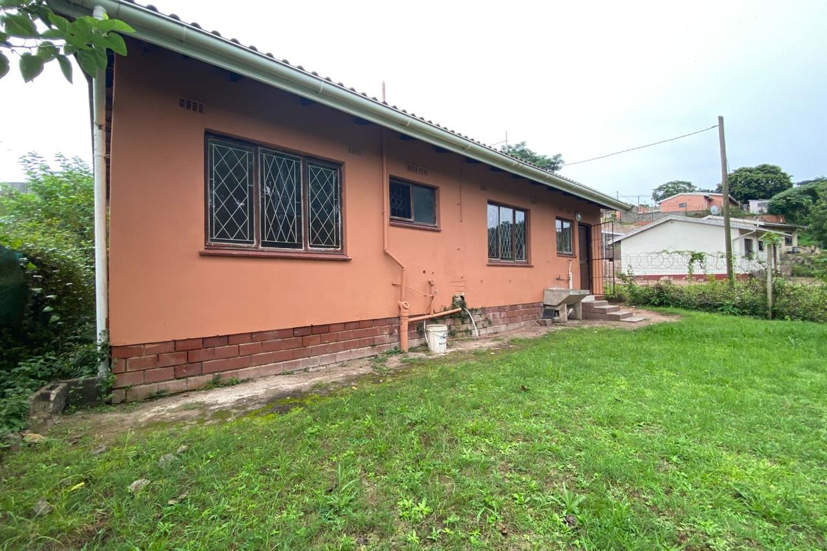 Rear exterior view of the house featuring a brick base, painted walls, diamond-pattern window frames, and an outdoor utility sink area.