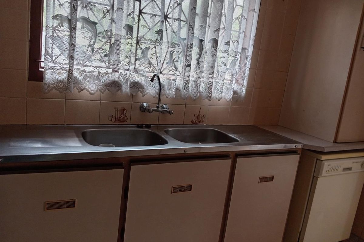 A dated kitchen area featuring a stainless steel double sink, tiled backsplash, and built-in cabinetry with integrated dishwasher space.