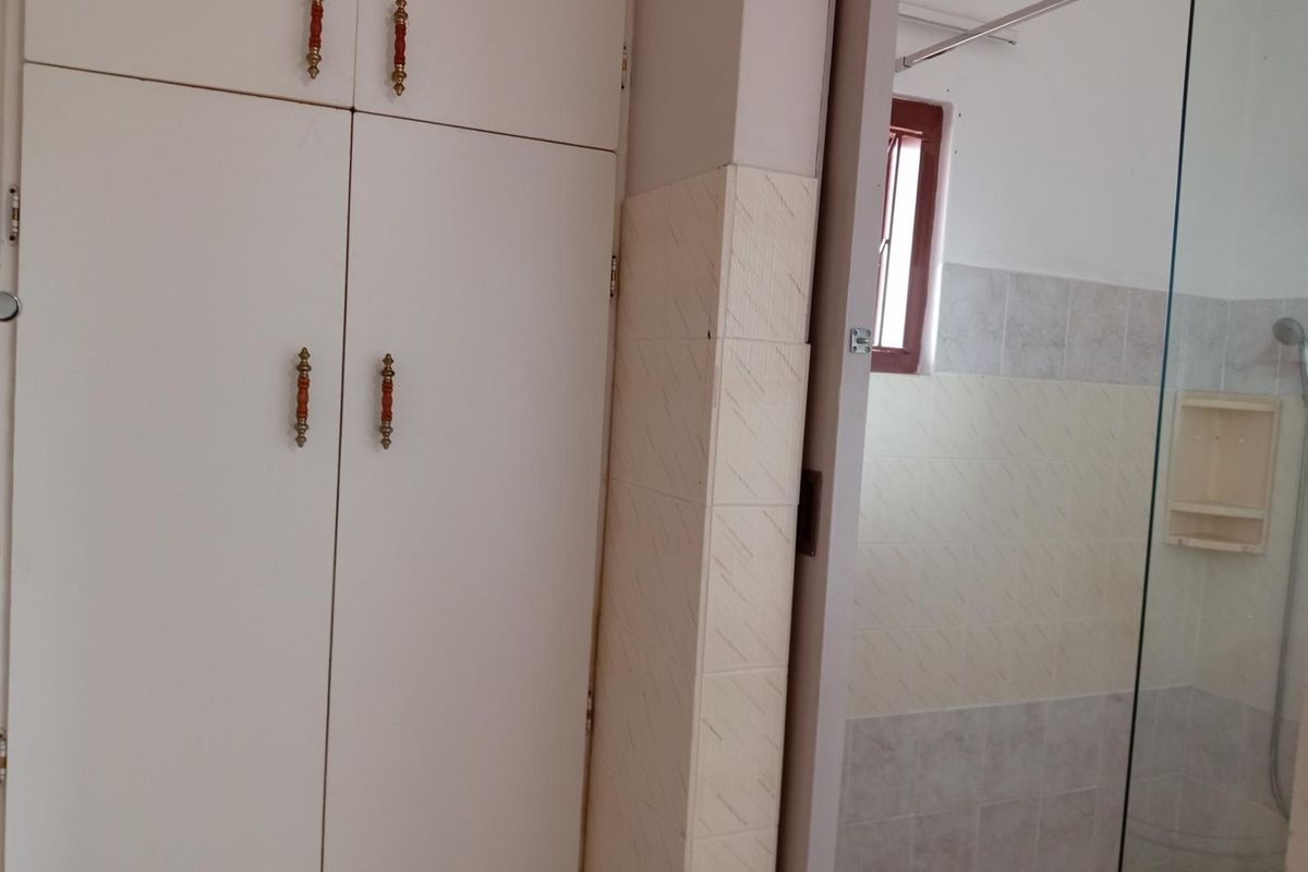 A bathroom featuring built-in storage cabinetry and a glass-enclosed shower area with tiled walls.