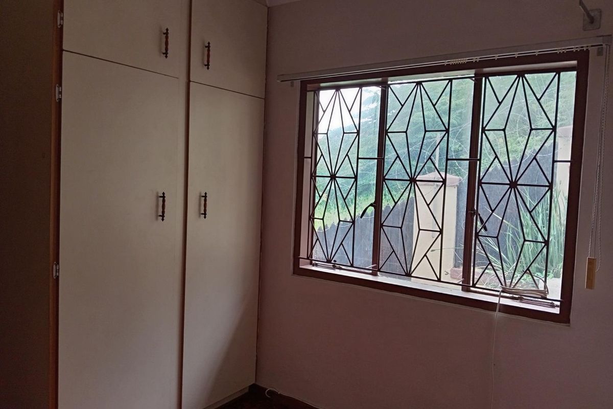 A bedroom featuring built-in floor-to-ceiling cupboards and a window fitted with decorative security burglar bars.
