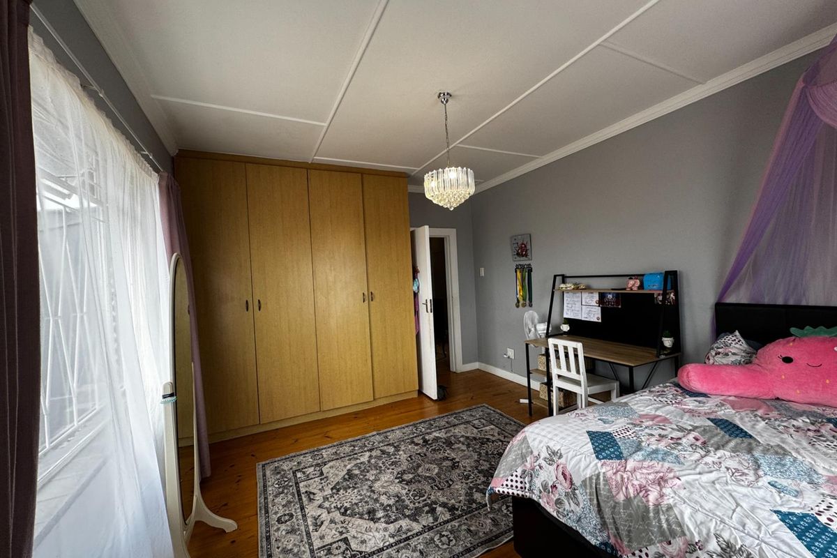 A bedroom featuring built-in wooden wardrobes, timber flooring, and a decorative chandelier, offering a functional and comfortable living space.
