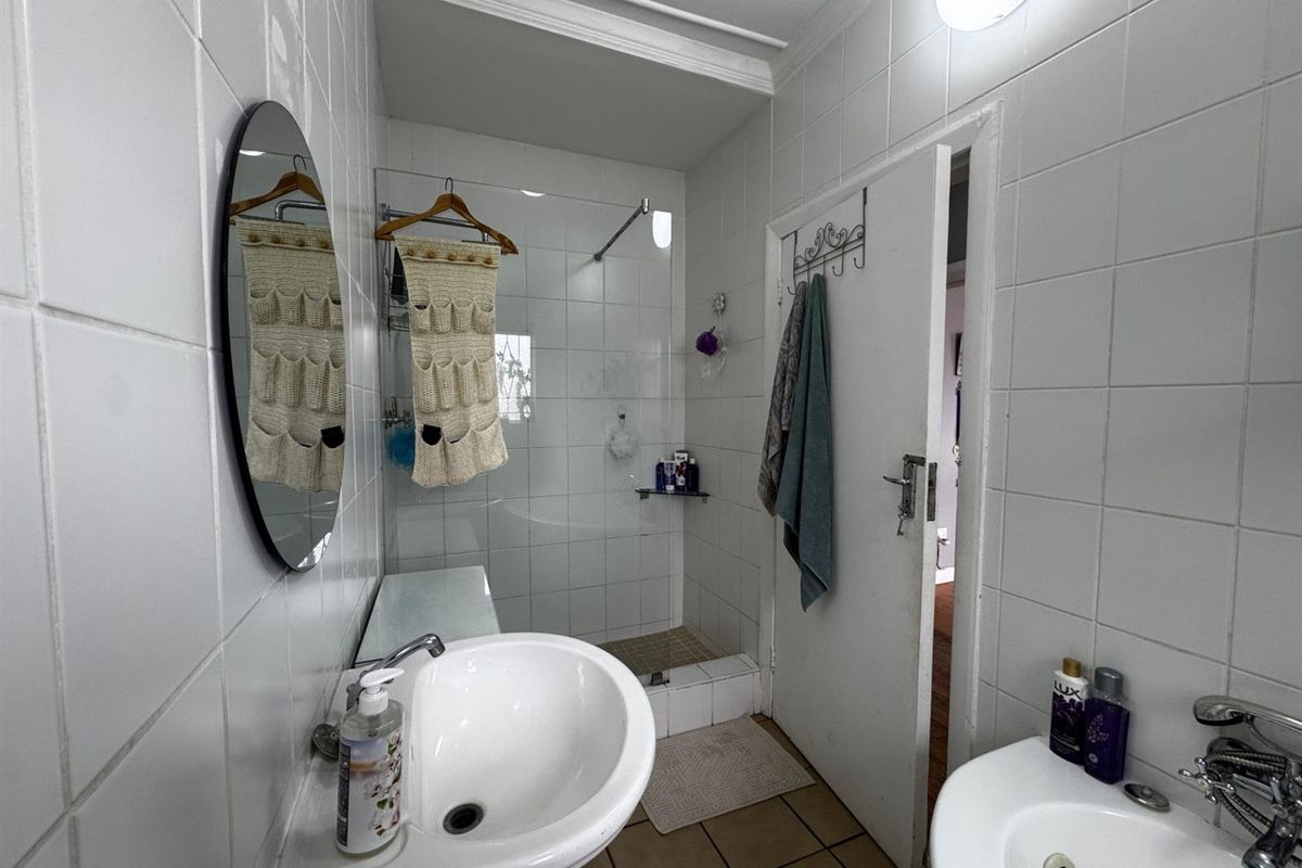 A functional bathroom featuring a walk-in shower with glass screen, pedestal basin, and tiled walls and flooring.