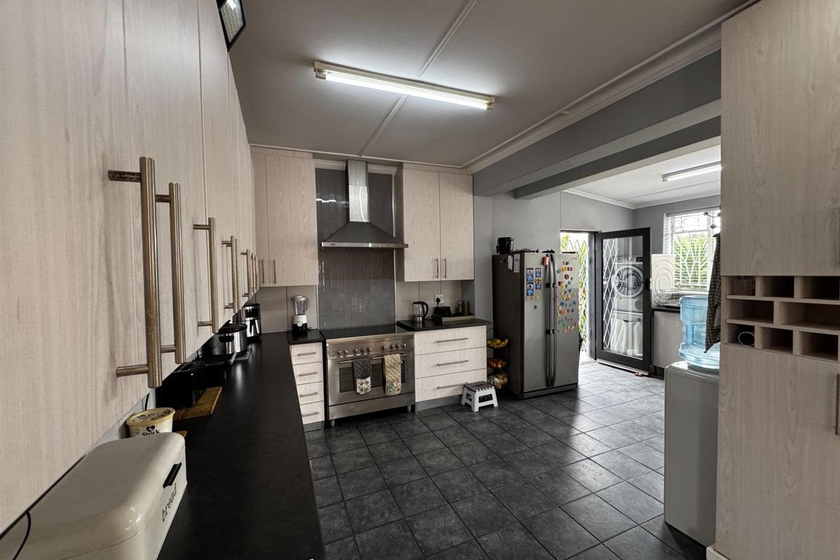 A functional kitchen featuring light wood-grain cabinetry, dark countertops, a stainless steel freestanding stove with extractor fan, and tiled flooring.