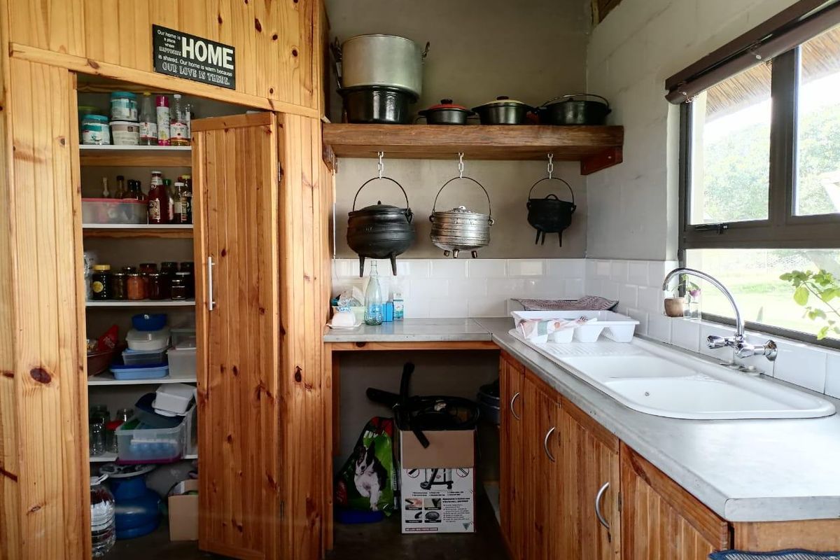 A rustic kitchen area featuring wooden cabinetry, a double basin sink, subway tile backsplash, and an integrated pantry storage space.