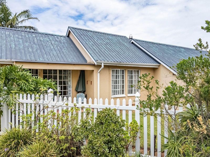 Rear view of a townhouse featuring a metal roof, white picket fencing, and a small patio area accessible through sliding glass doors.