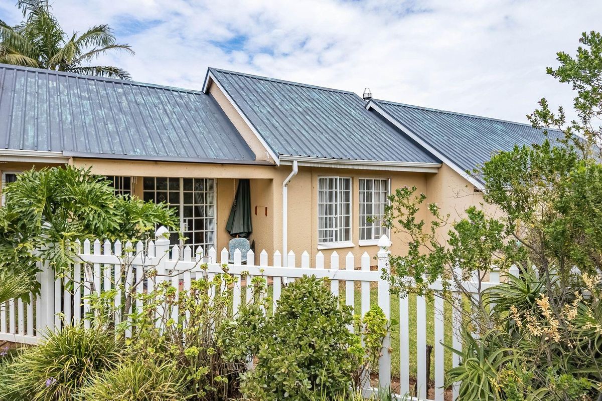 Rear view of a townhouse featuring a metal roof, white picket fencing, and a small patio area accessible through sliding glass doors.