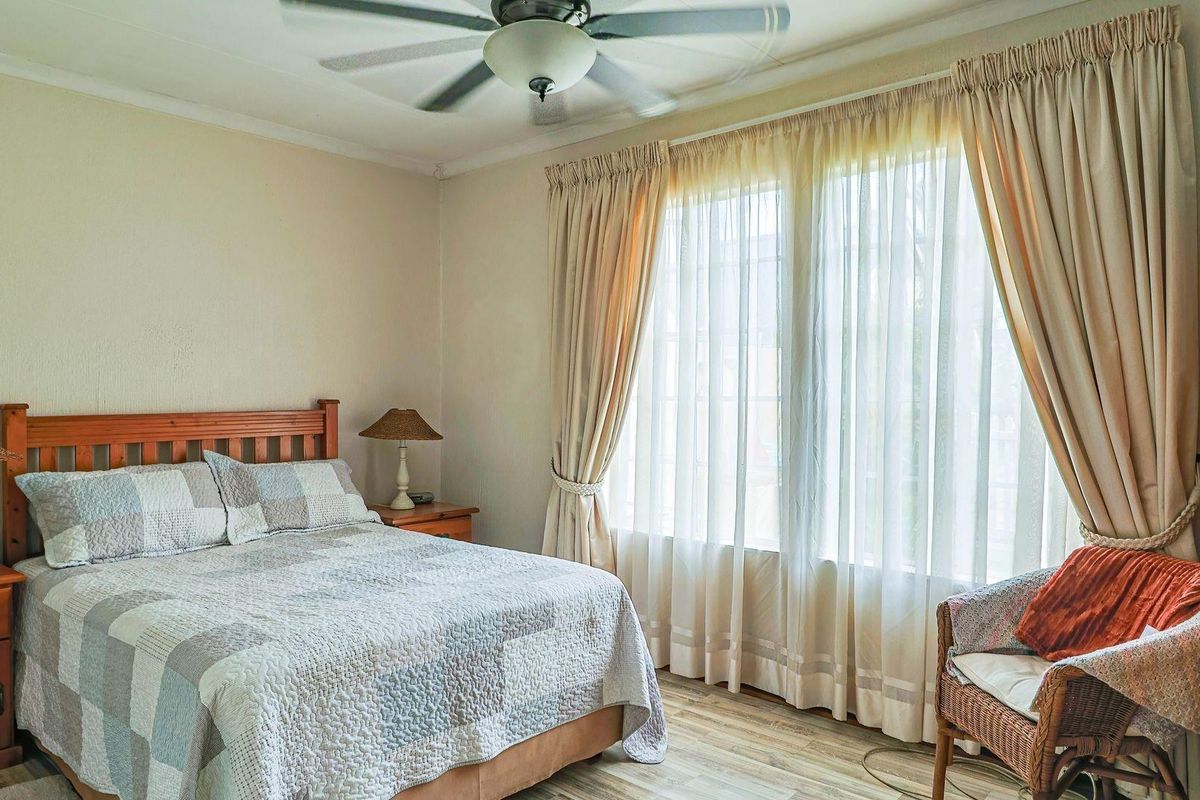 A well-lit bedroom featuring laminate flooring and a ceiling fan, offering a comfortable and functional living space.