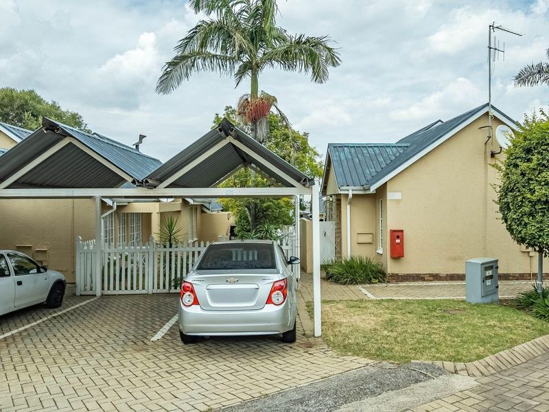 Front exterior view of a townhouse complex featuring a paved driveway, covered carport parking, and a small garden area.