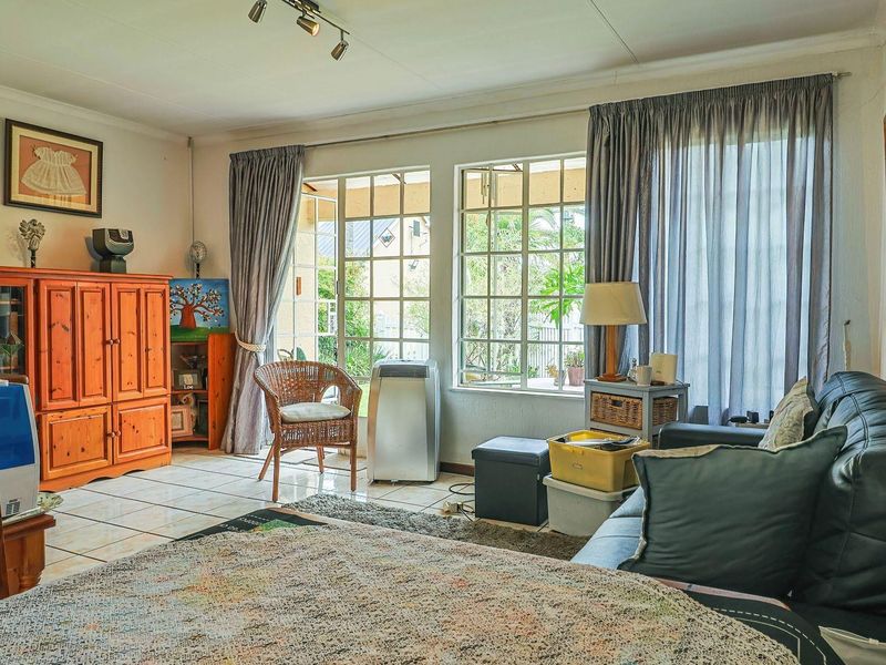 A living room featuring tiled flooring, track lighting, and large windows with access to an outdoor patio area.