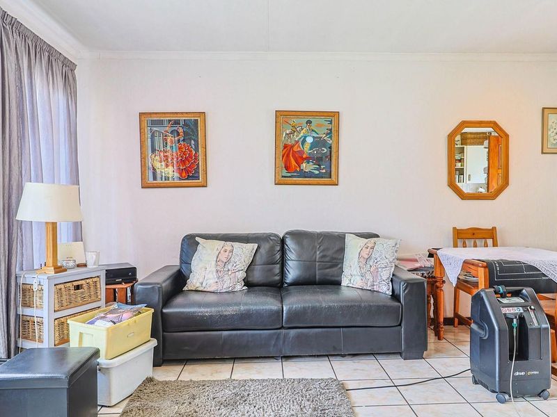 A living room area featuring tiled flooring and a large window, providing a functional space with neutral wall finishes.
