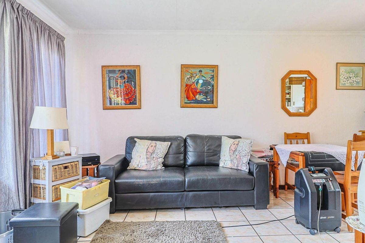 A living room area featuring tiled flooring and a large window, providing a functional space with neutral wall finishes.
