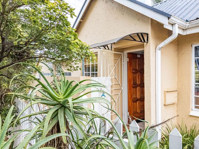 Front entrance of the townhouse featuring a timber door, security gate, protective awning, and a white picket fence.