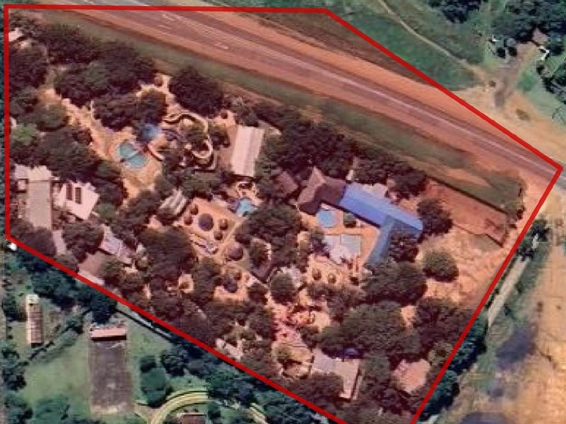 An aerial view of a property complex featuring multiple buildings, swimming pools, and extensive landscaped grounds situated near a main road.
