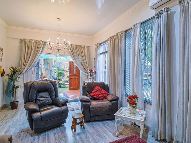 A bright living room featuring laminate flooring, a decorative chandelier, and direct access to an outdoor patio area through a glass door.