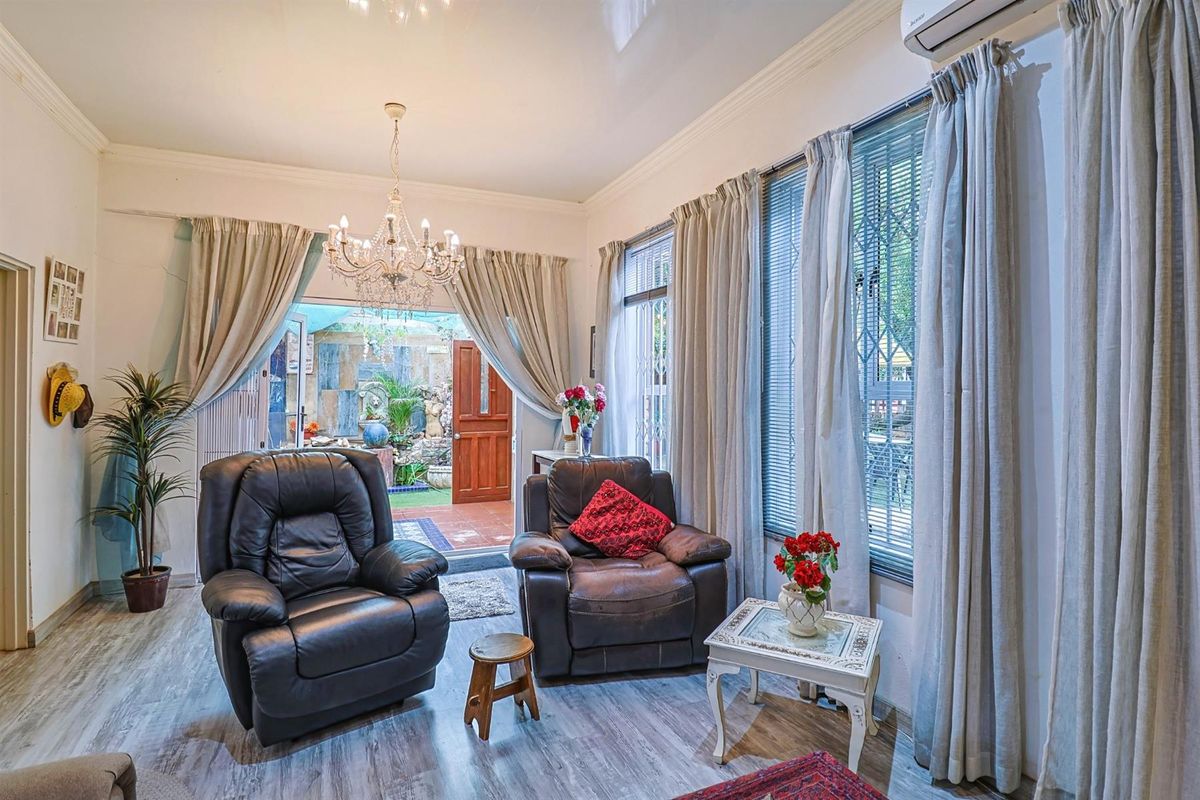A bright living room featuring laminate flooring, a decorative chandelier, and direct access to an outdoor patio area through a glass door.