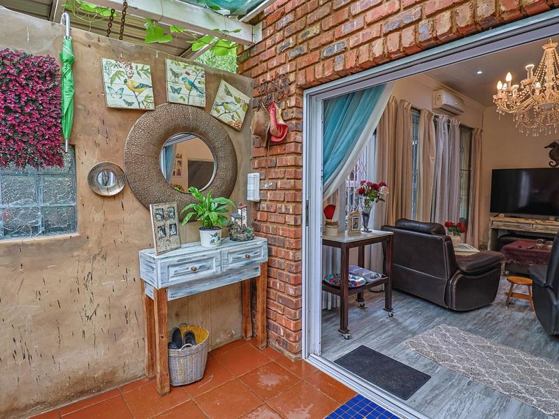 A covered patio area featuring exposed brickwork, terracotta tiling, and a glass sliding door providing seamless access to the interior living space.