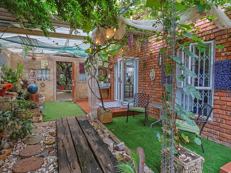 A rustic covered patio area featuring exposed brick walls, artificial grass, and a timber sleeper walkway, providing a cozy outdoor entertainment space.