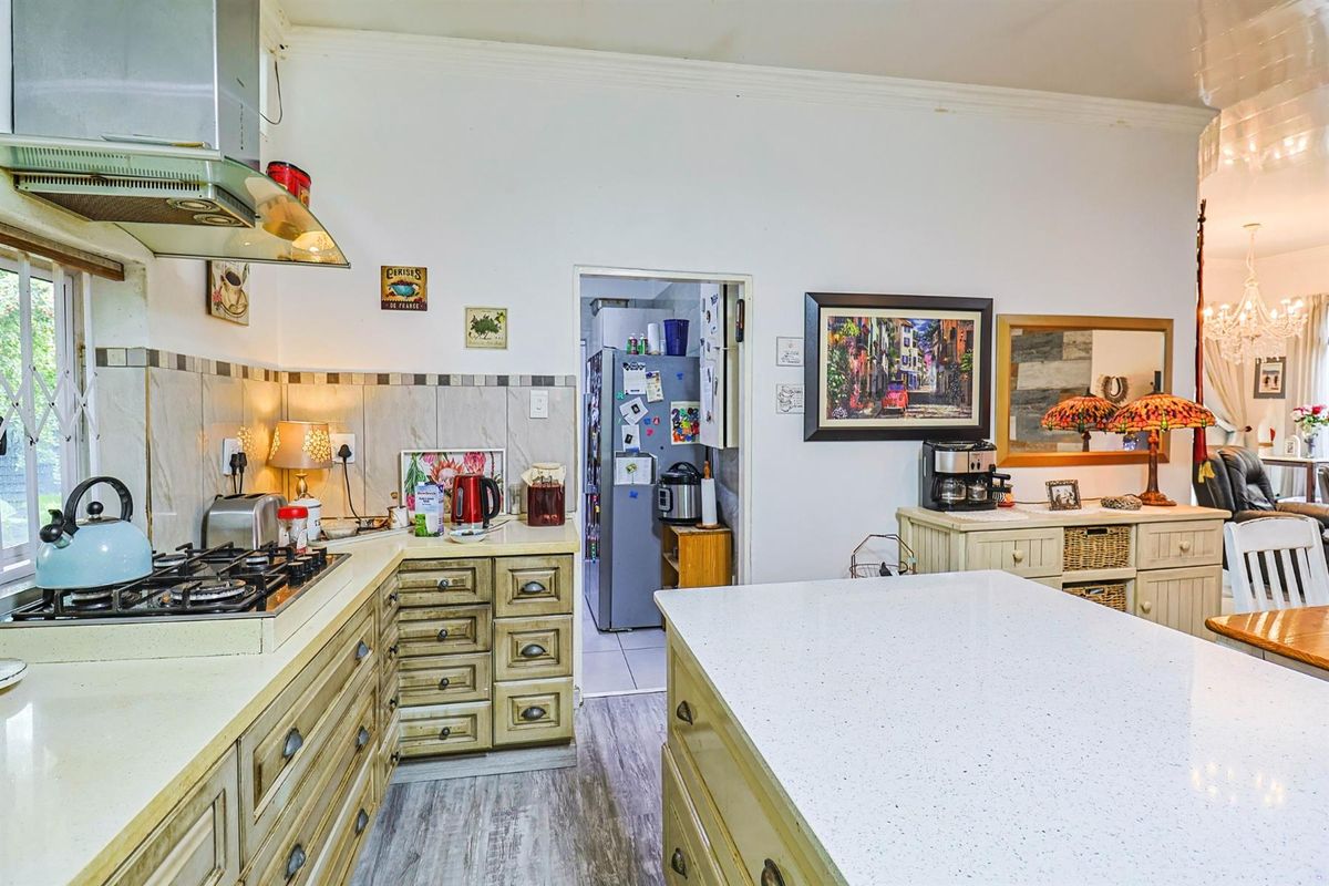 A functional kitchen featuring a central island, gas hob with extractor, stone countertops, and ample cabinetry, with an adjacent scullery area.