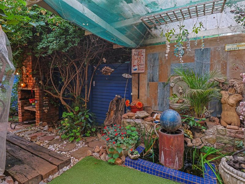 Outdoor patio area featuring a brick built-in braai, a decorative water feature, and timber decking under a shade-netted cover.