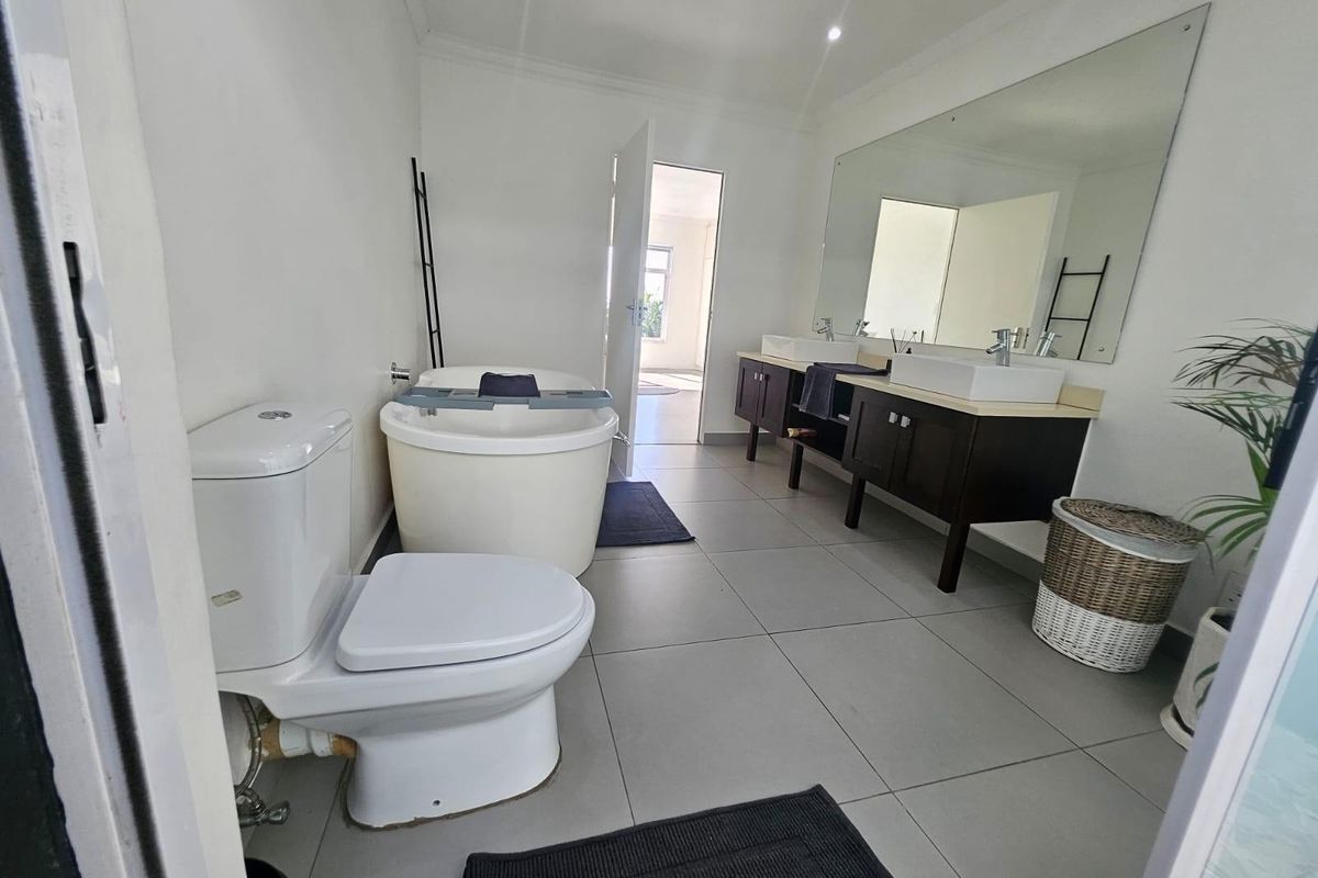 A modern bathroom featuring a double vanity with vessel sinks, a freestanding bathtub, a toilet, and large wall-mounted mirrors.
