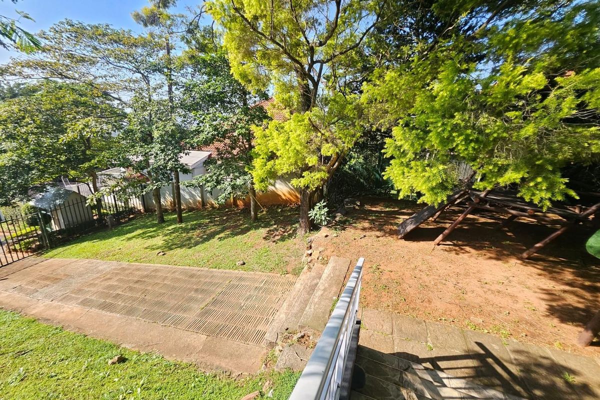 A spacious rear garden featuring mature trees, a paved walkway, and a tiered lawn area, providing a private outdoor space.