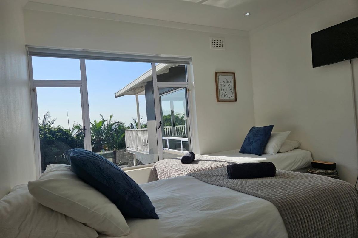 A bright bedroom featuring large windows with views of the exterior balcony and surrounding greenery, equipped with recessed ceiling lighting.