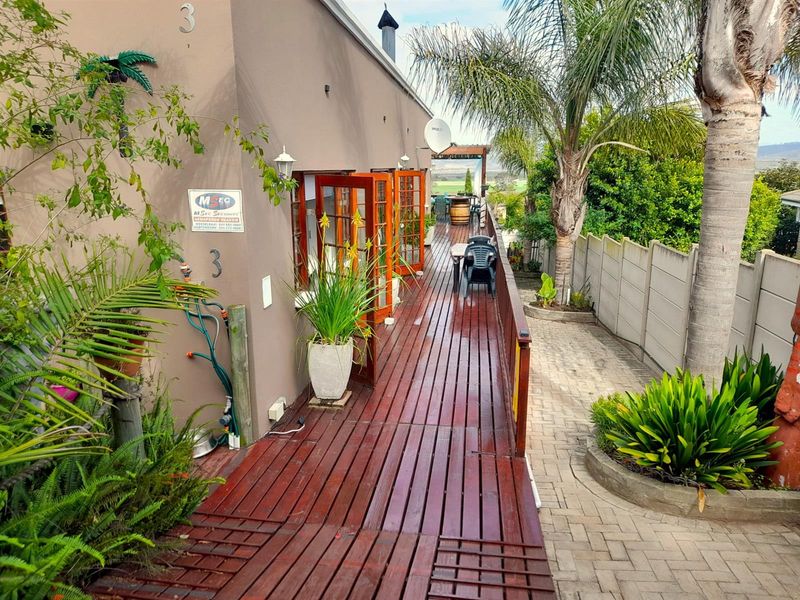 A long timber deck patio featuring multiple sets of french doors, providing outdoor access alongside a paved walkway and garden area.