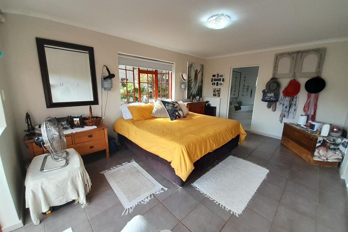 A spacious bedroom featuring tiled flooring and timber-framed windows, offering a functional layout with direct access to an adjoining room.