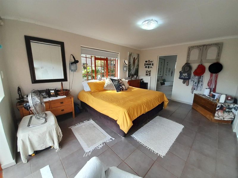 A spacious bedroom featuring tiled flooring and timber-framed windows, offering a functional layout with direct access to an adjoining room.
