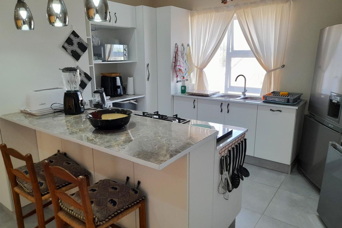 Modern kitchen featuring white cabinetry, stone-look countertops, a built-in gas hob, and a double basin sink with ample natural light.