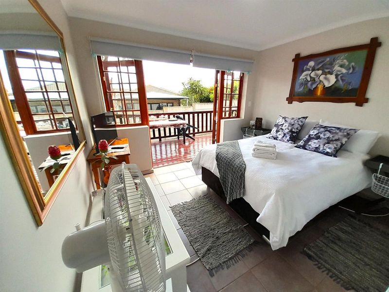 A bedroom featuring tiled flooring and timber-framed glass doors that open onto a private balcony, providing natural light and outdoor access.