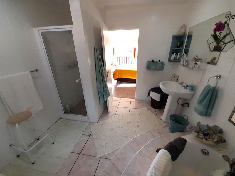 A functional bathroom featuring a pedestal sink, shower enclosure, and tiled flooring, with direct access to an adjacent bedroom.