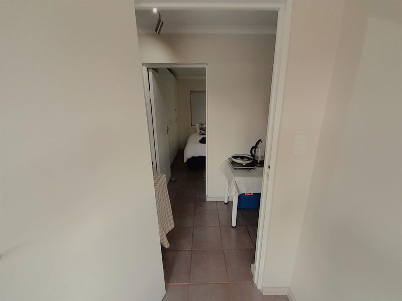 A view through a doorway into a tiled hallway leading to a bedroom area with neutral wall finishes.